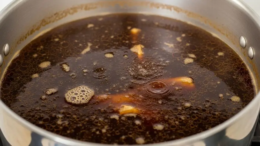 "Grande panela profissional contendo fundo escuro de vitela boi no meio do processo de extração longa no estágio frémissement a superfície do líquido mostra o tremor suave característico bolhas quase imperceptíveis nas bordas não é fervura vigorosa a cor já é âmbar-marrom profunda indicando que os compostos de Maillard da tostagem estão se dissolvendo no caldo ossos tostados visíveis através do líquido translúcido escuro sem tampa vapor subindo suavemente"