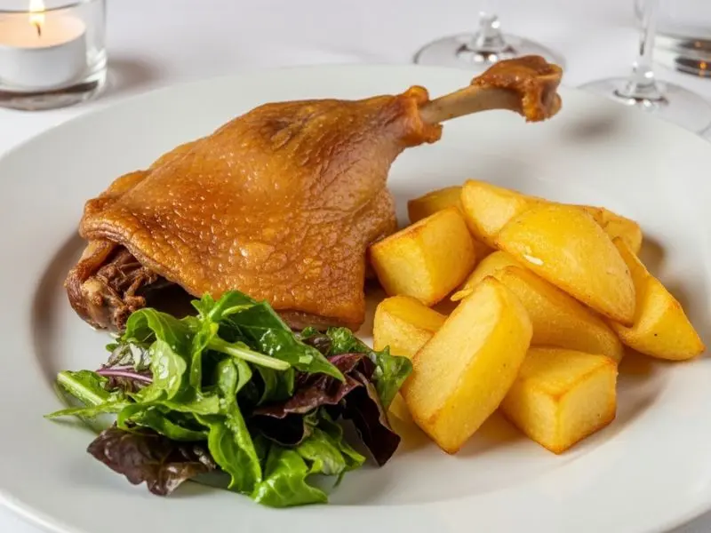 "Prato completo de confit de canard com coxa de pato de pele crocante dourada pommes sarladaises e folhas amargas com vinagrete em apresentação de restaurante francês"
