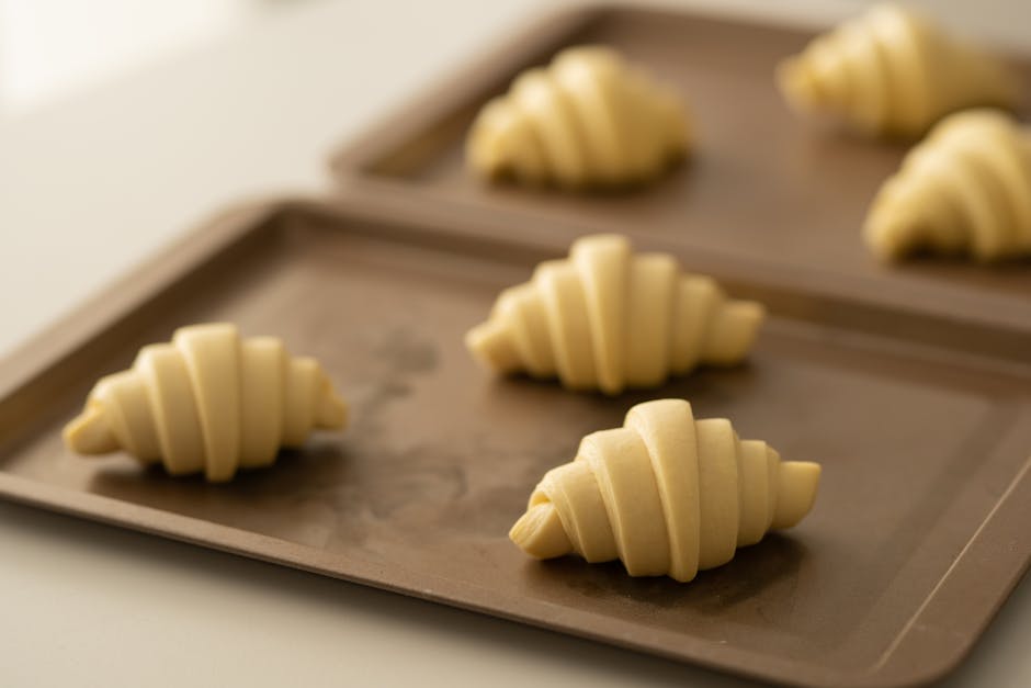 Freshly prepared croissant dough ready for baking, placed on brown trays.