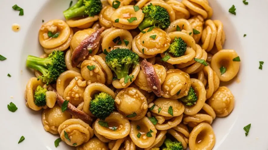 "close-up de orecchiette com pedaços de brócolis dentro das cavidades da massa cobertos por molho dourado de alho e anchova"