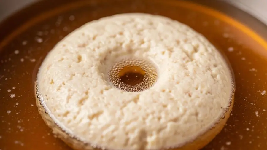 "raft de clarificação do consommé formado na superfície da panela com orifício central e líquido âmbar cristalino visível embaixo" 